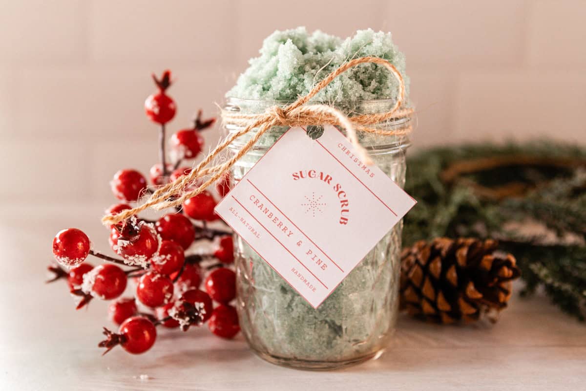 A jar of Christmas tree sugar scrub with pinecones and red berries.