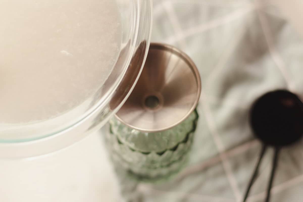 Pouring soap scum remover into a green glass spray bottle.