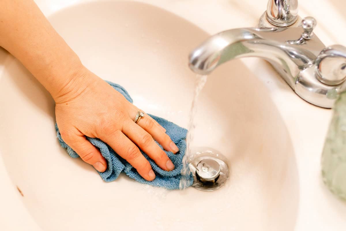 Rinsing a bathroom sink with water and a microfiber cloth.