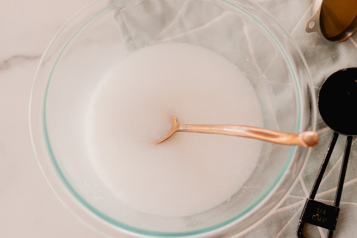 A glass bowl with soap scum mixture and a spoon in it.