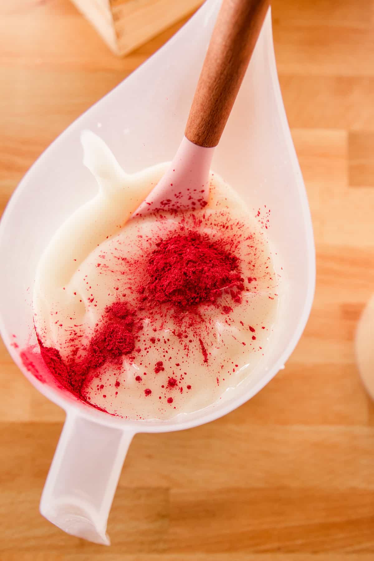 A pitcher of melted soap mixture with red mica powder on top. 