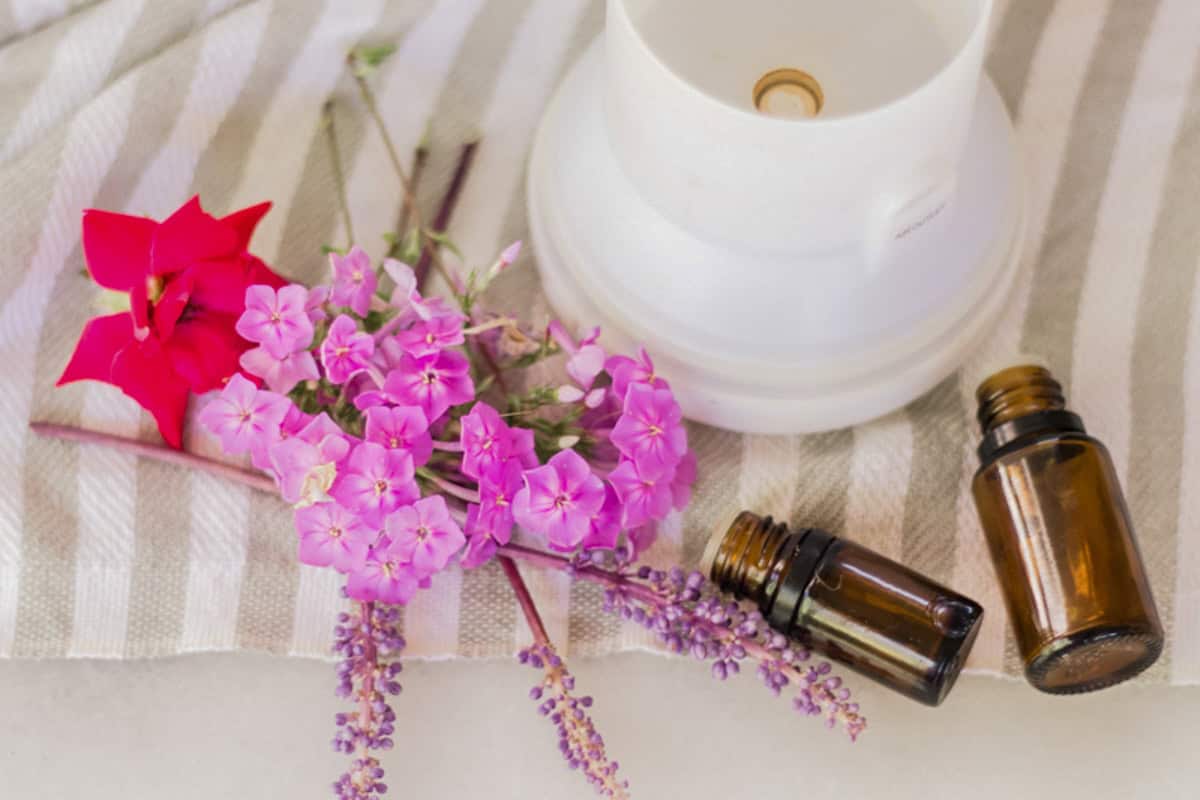 An essential oil diffuser with essential oil bottles and fresh flowers.