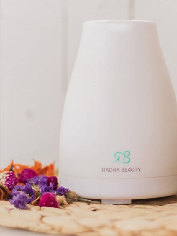An essential oil diffuser on a wicker placemat with fresh flowers.