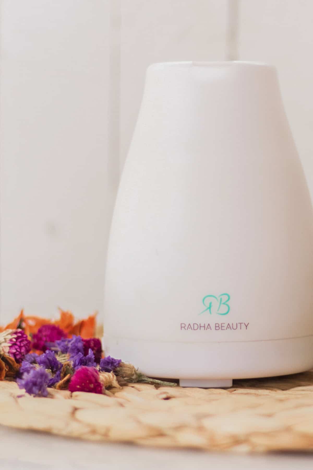 An essential oil diffuser on a wicker placemat with fresh flowers.
