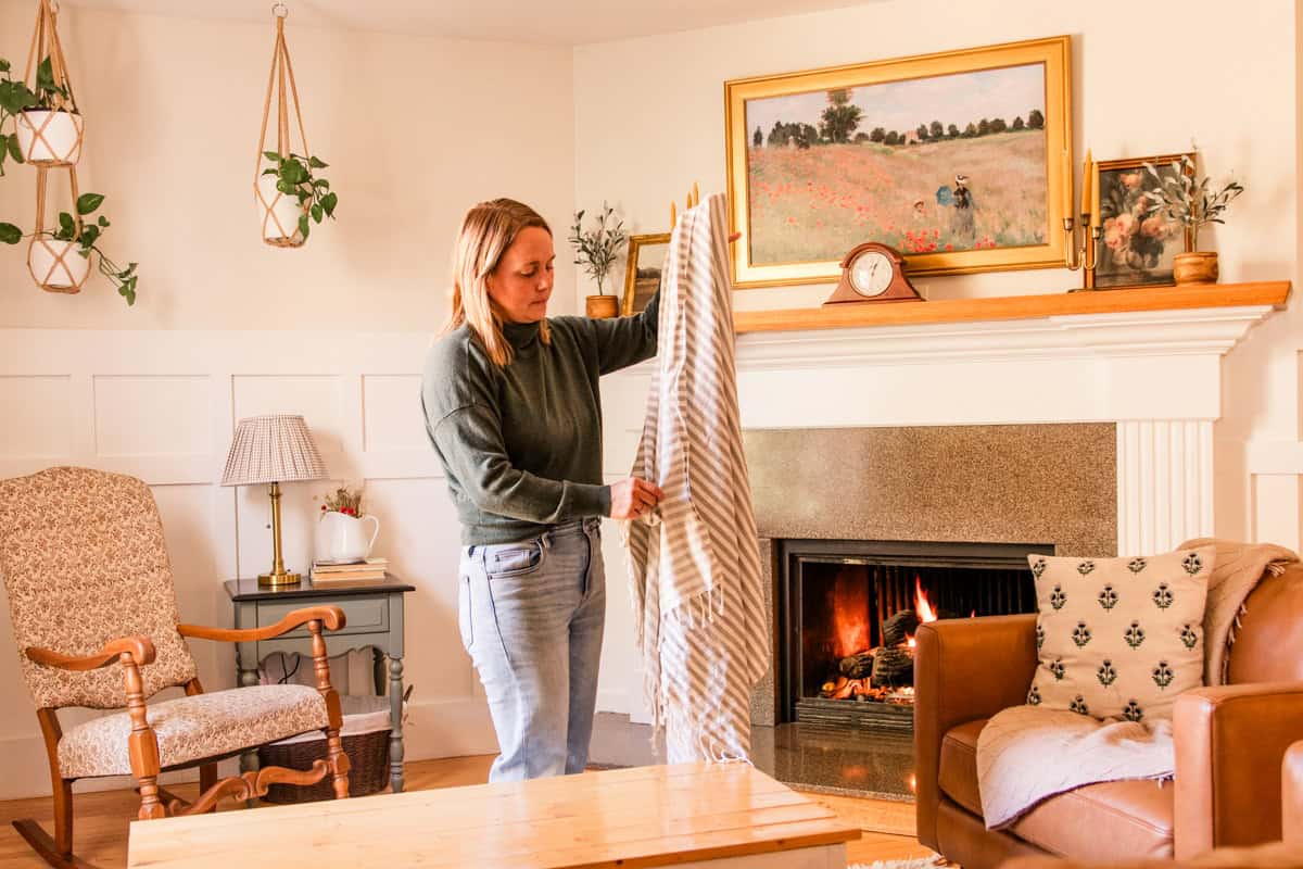 Holding a decorative blanket up to throw over a small chair. 