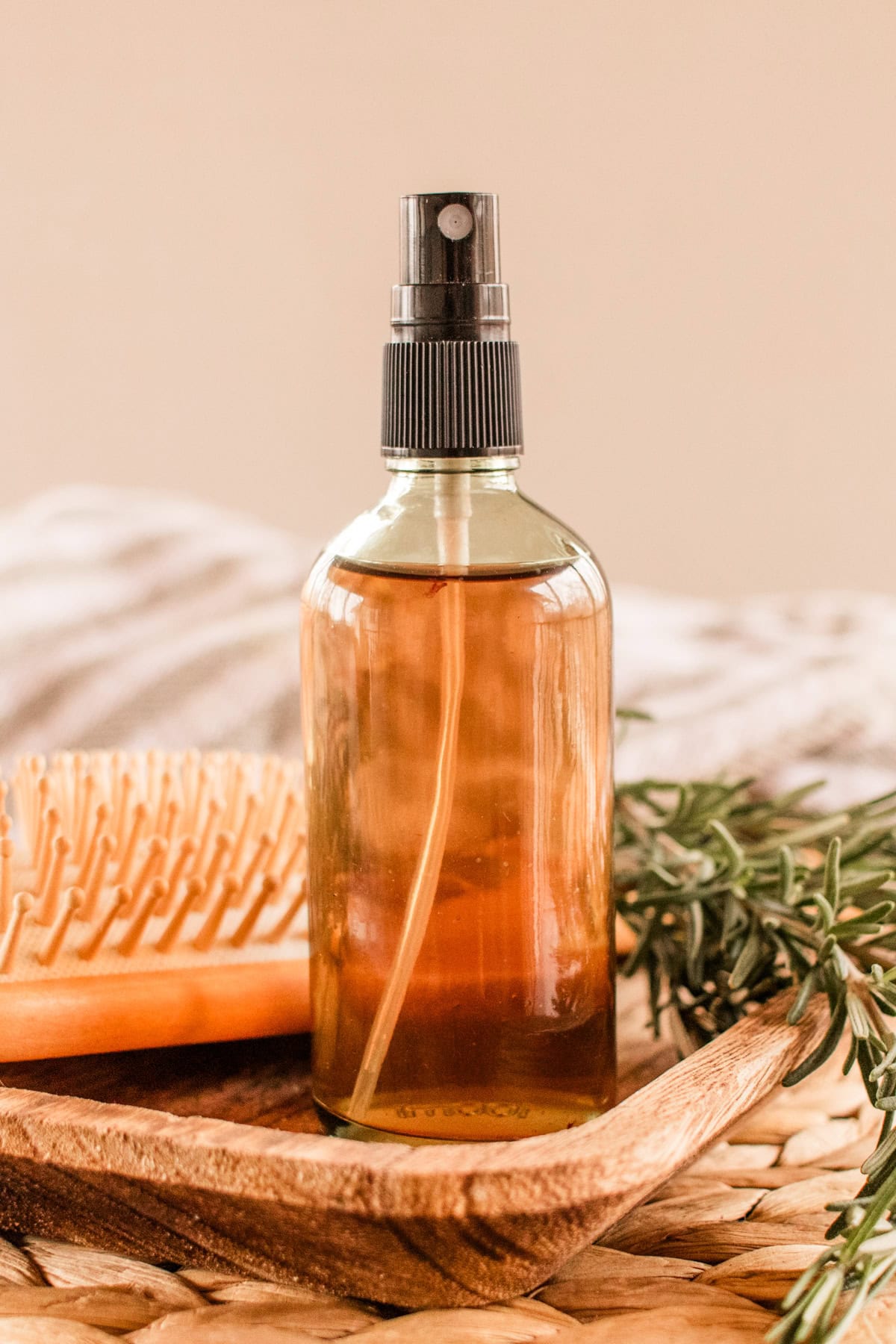 Homemade rosemary water spray on a wooden tray with a comb and greenery around it. 