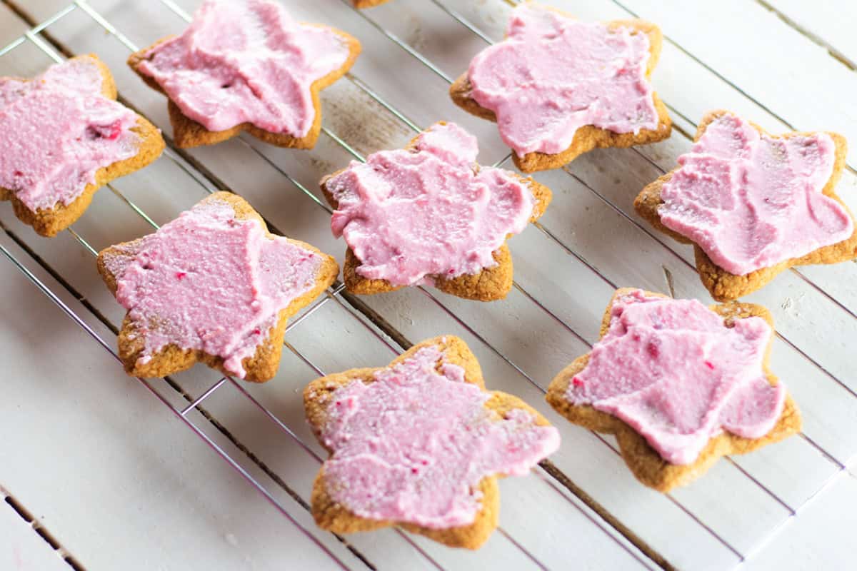 Paleo sugar cookies with pink frosting on a cooling rack.