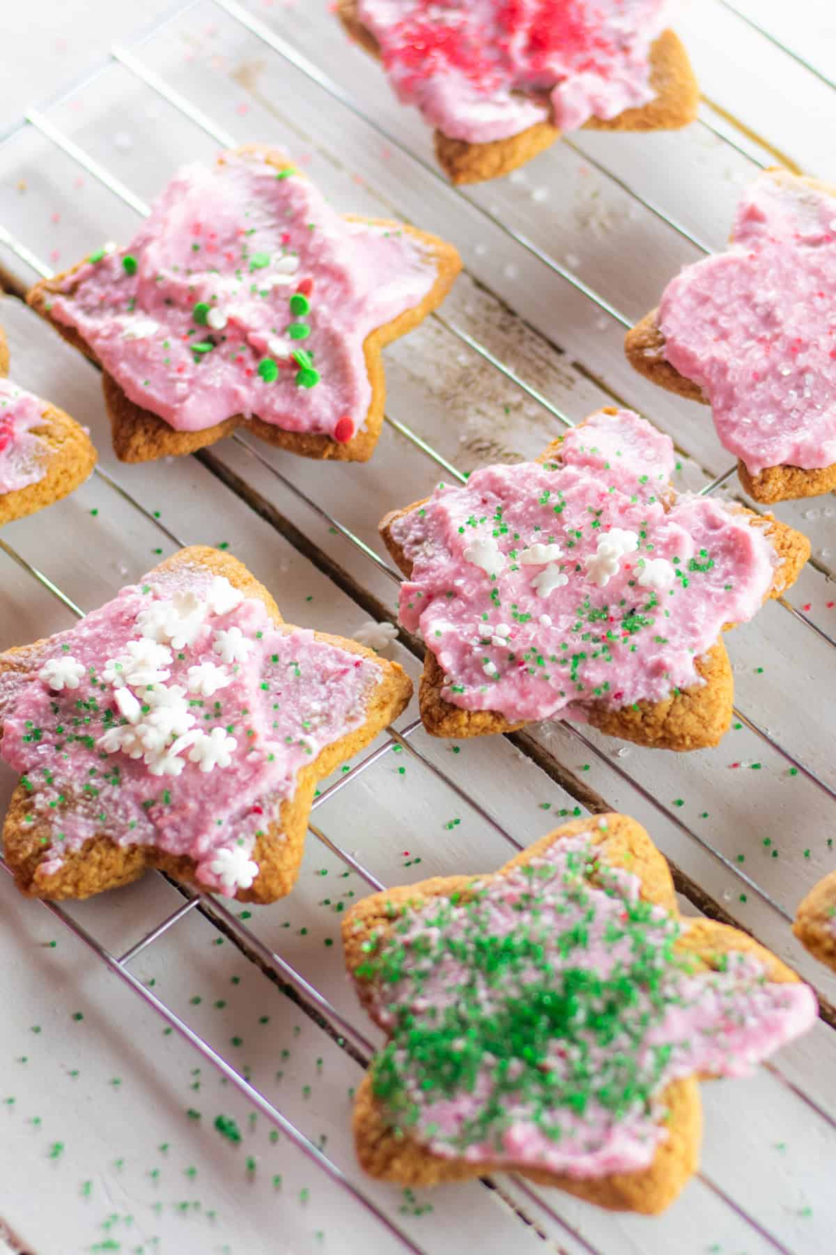 Paleo sugar cookies on a cooling rack with pink and frosting and sprinkles.