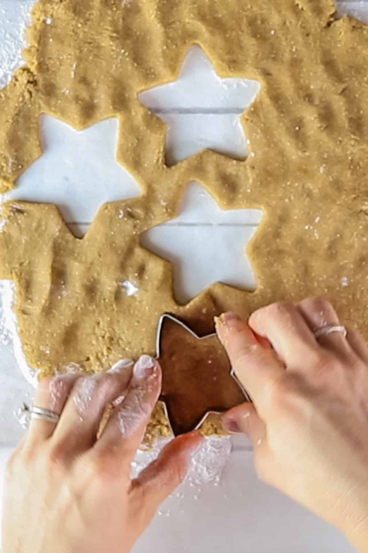 Cutting sugar cookies out of rolled-out batter with a star-shaped cookie cutter.