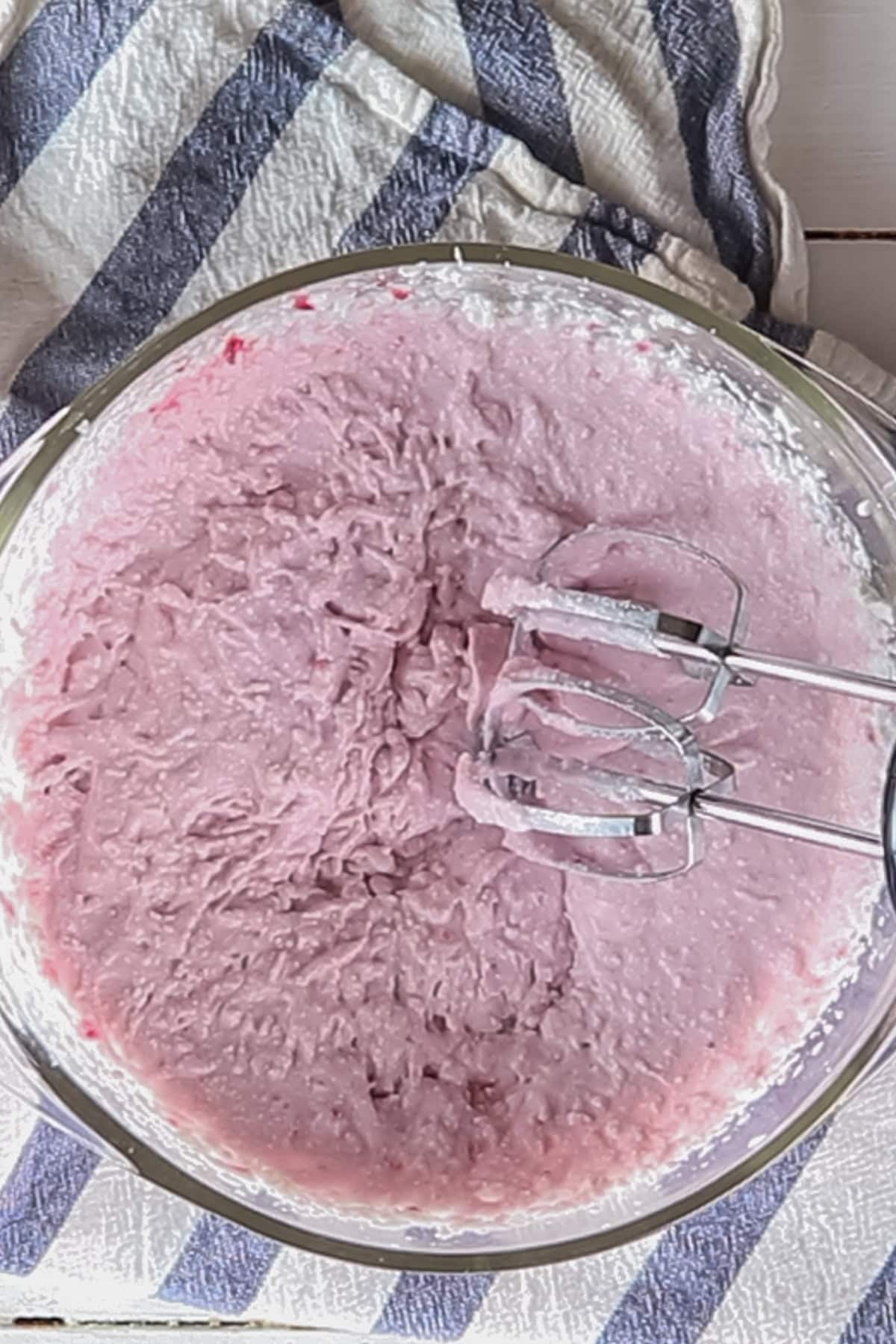 Mixing pink coconut cream frosting in a mixing bowl with a handheld mixer.
