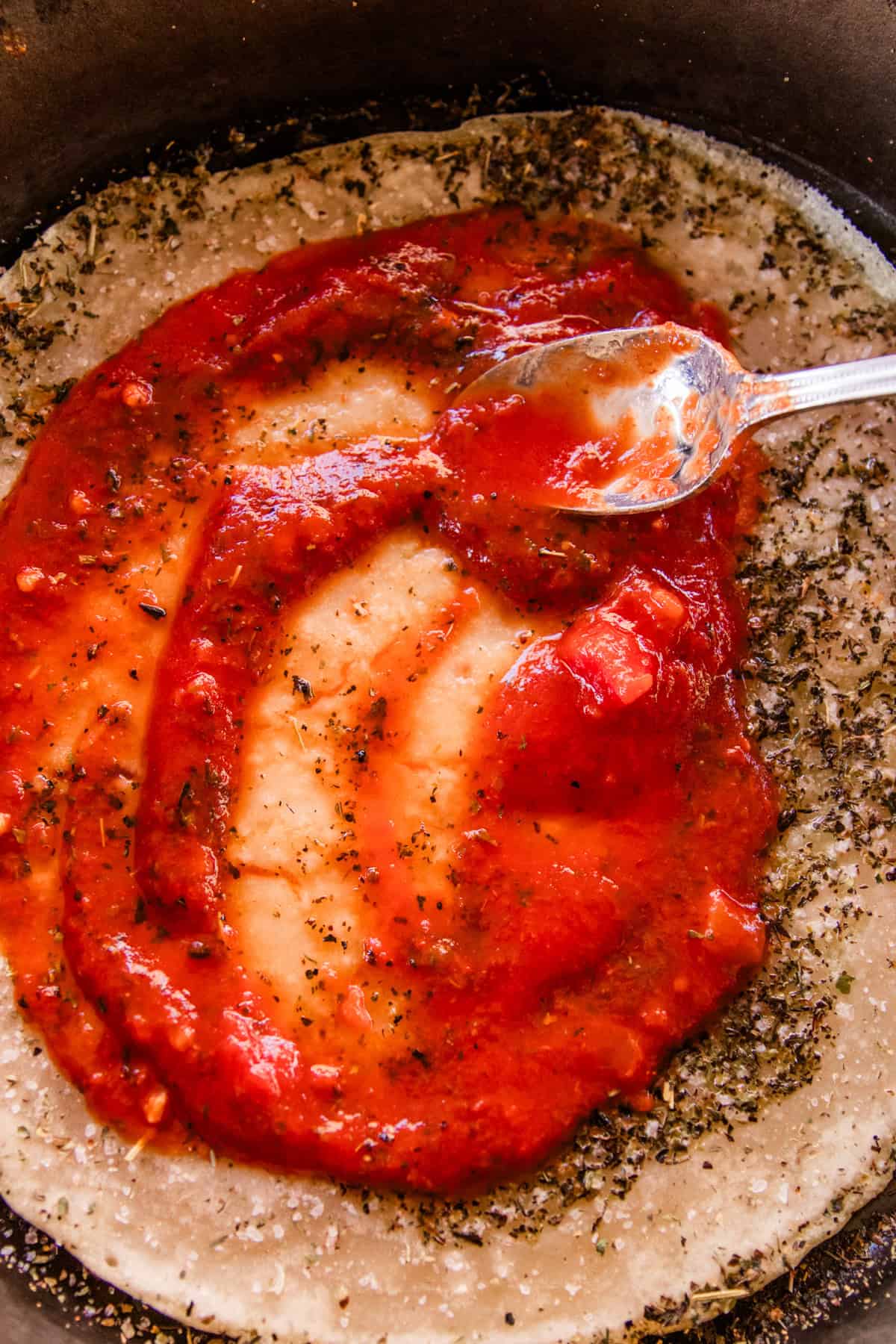 Spreading pizza sauce on a sourdough pizza crust.