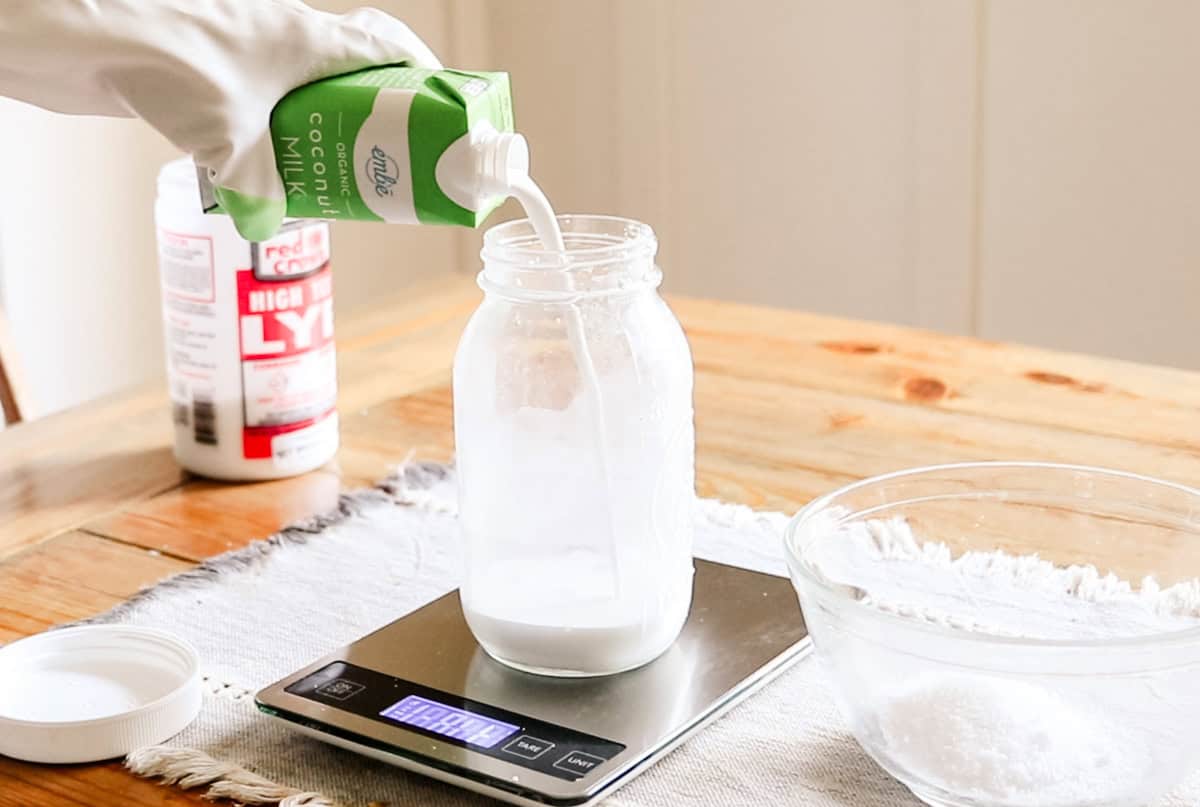 Pouring coconut milk into a jar sitting on a kitchen scale.