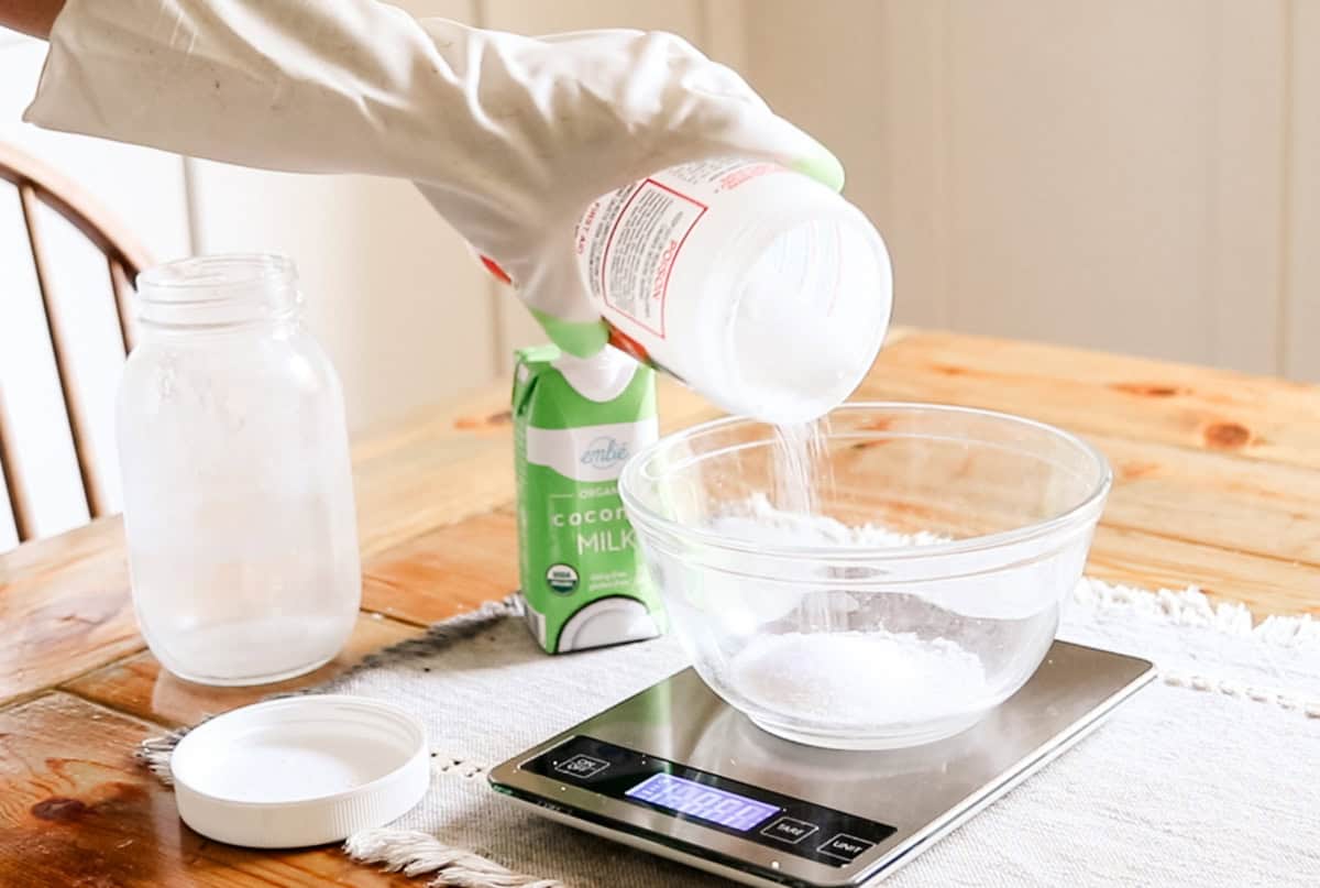 Pouring lye into a bowl sitting on a kitchen scale.