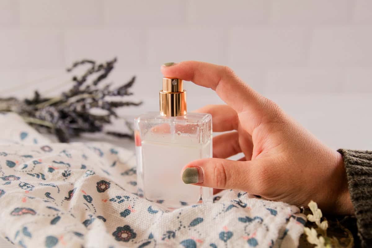A hand holding a bottle of homemade perfume on a floral towel.