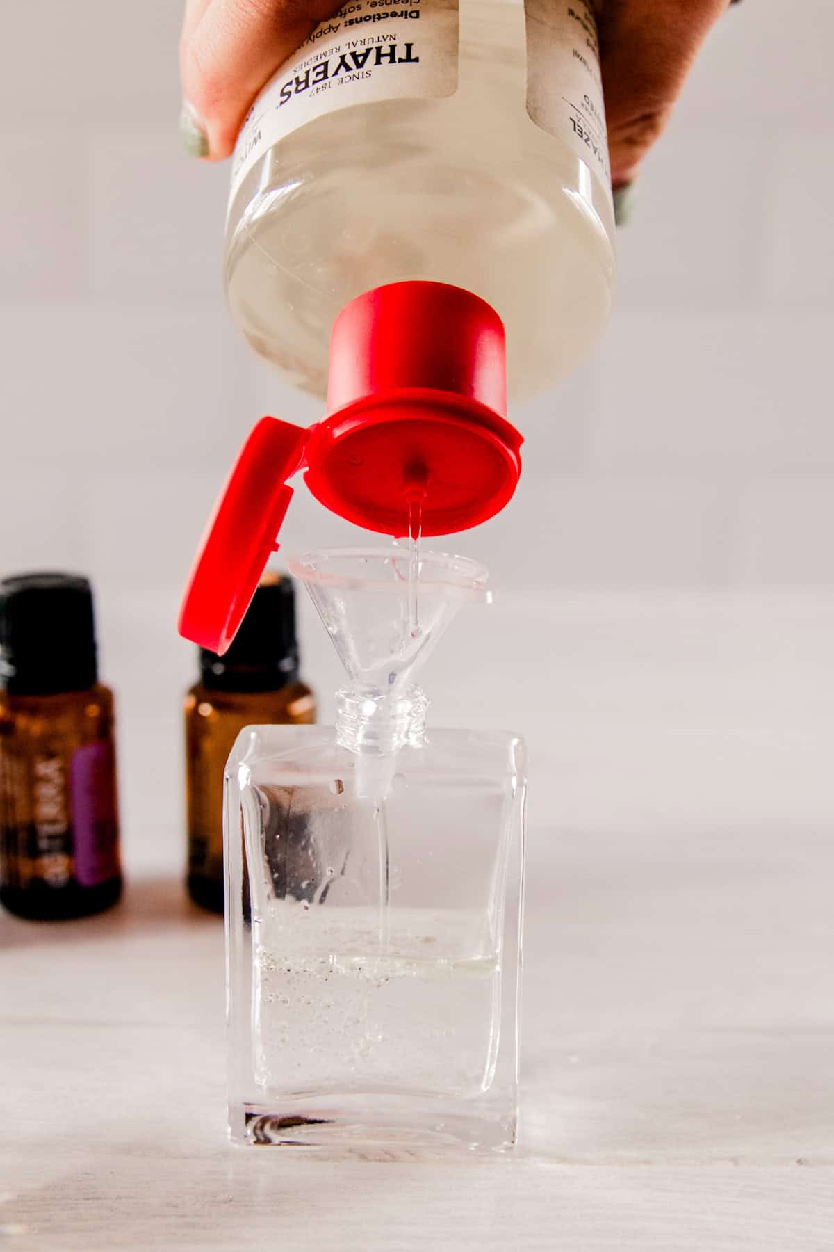 Squirting witch hazel into a glass perfume bottle.