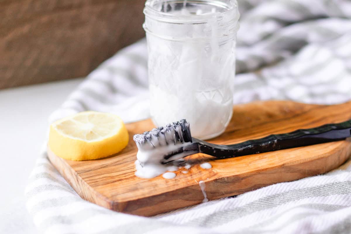 A jar of grout cleaner sitting on a wooden board with a lemon and a scrub brush.
