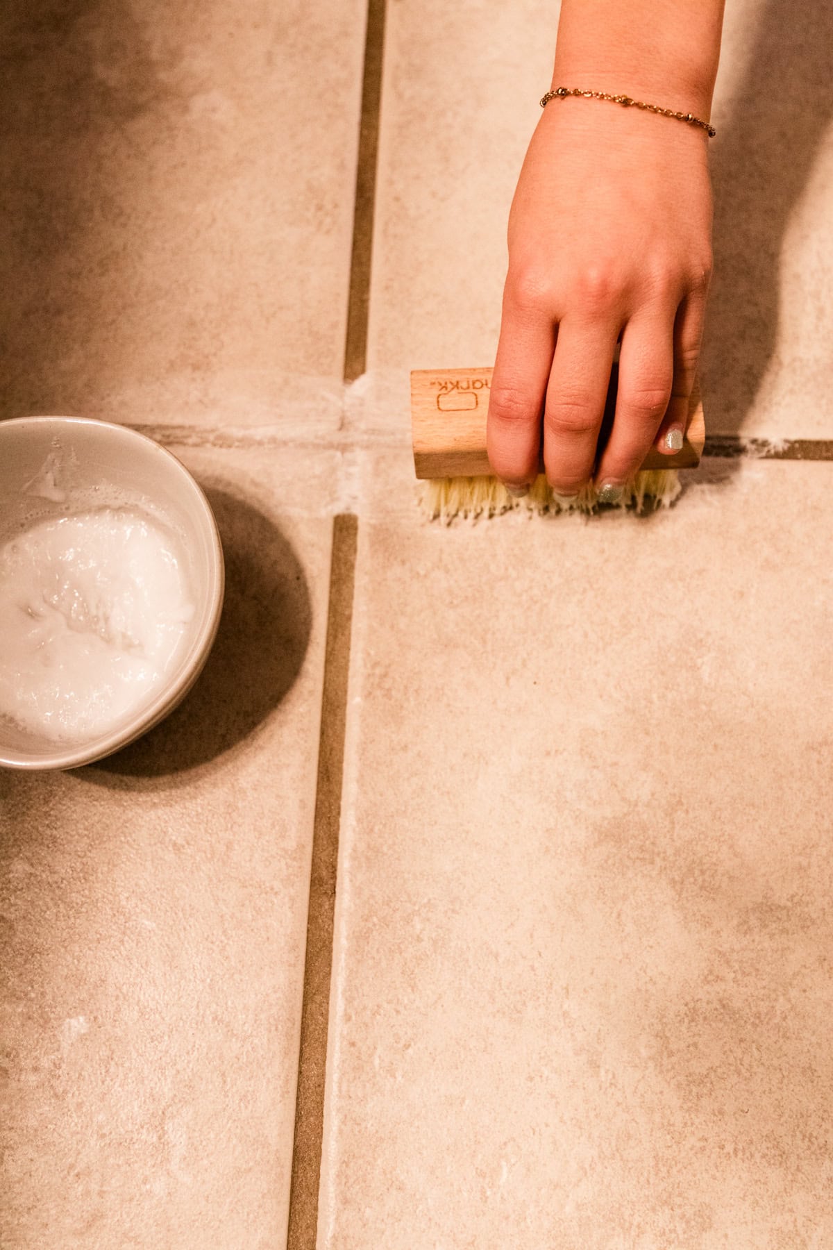 Scrubbing a grout line with homemade grout cleaner.