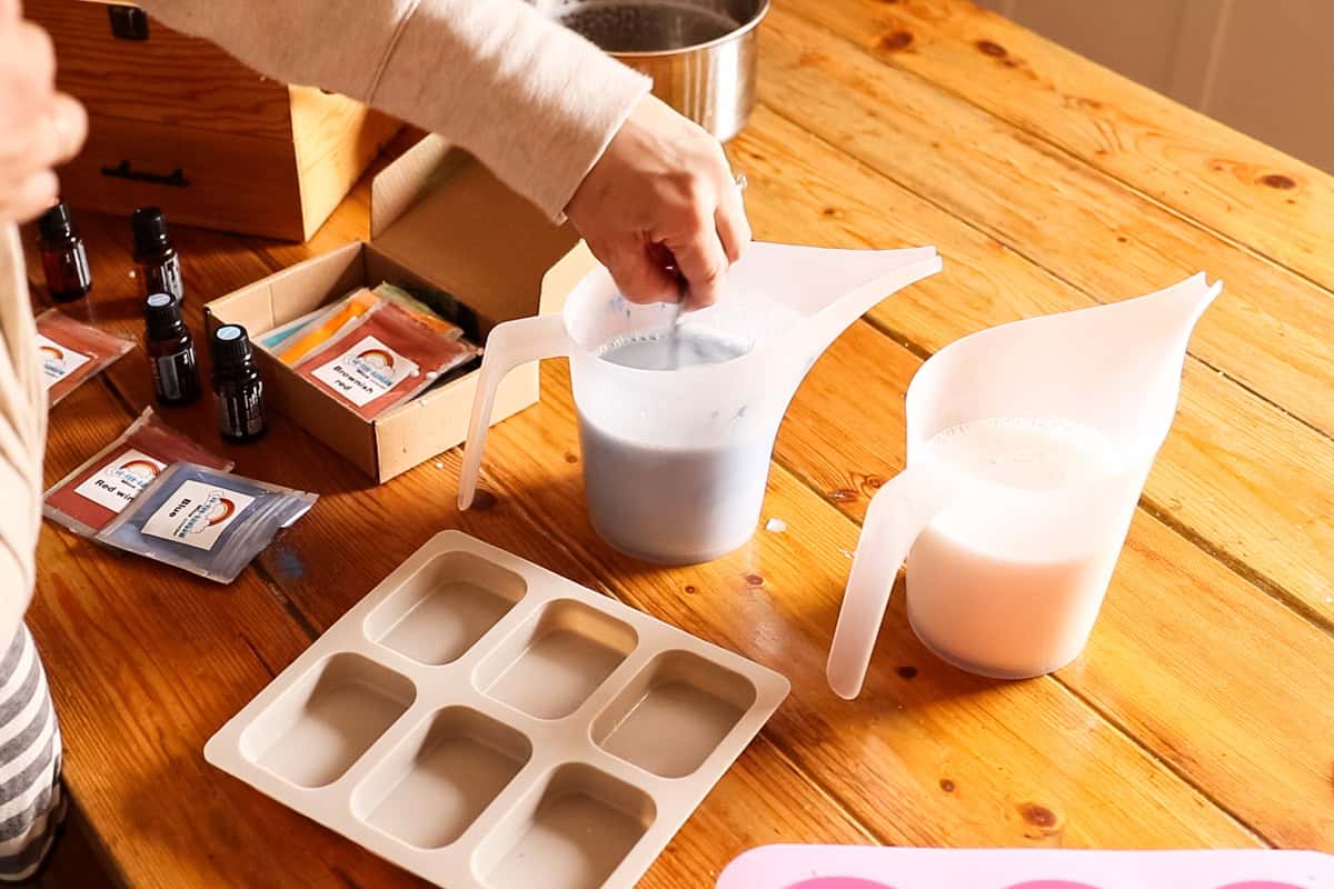 Stirring blue mica powder into one plastic pitcher of melted soap base.