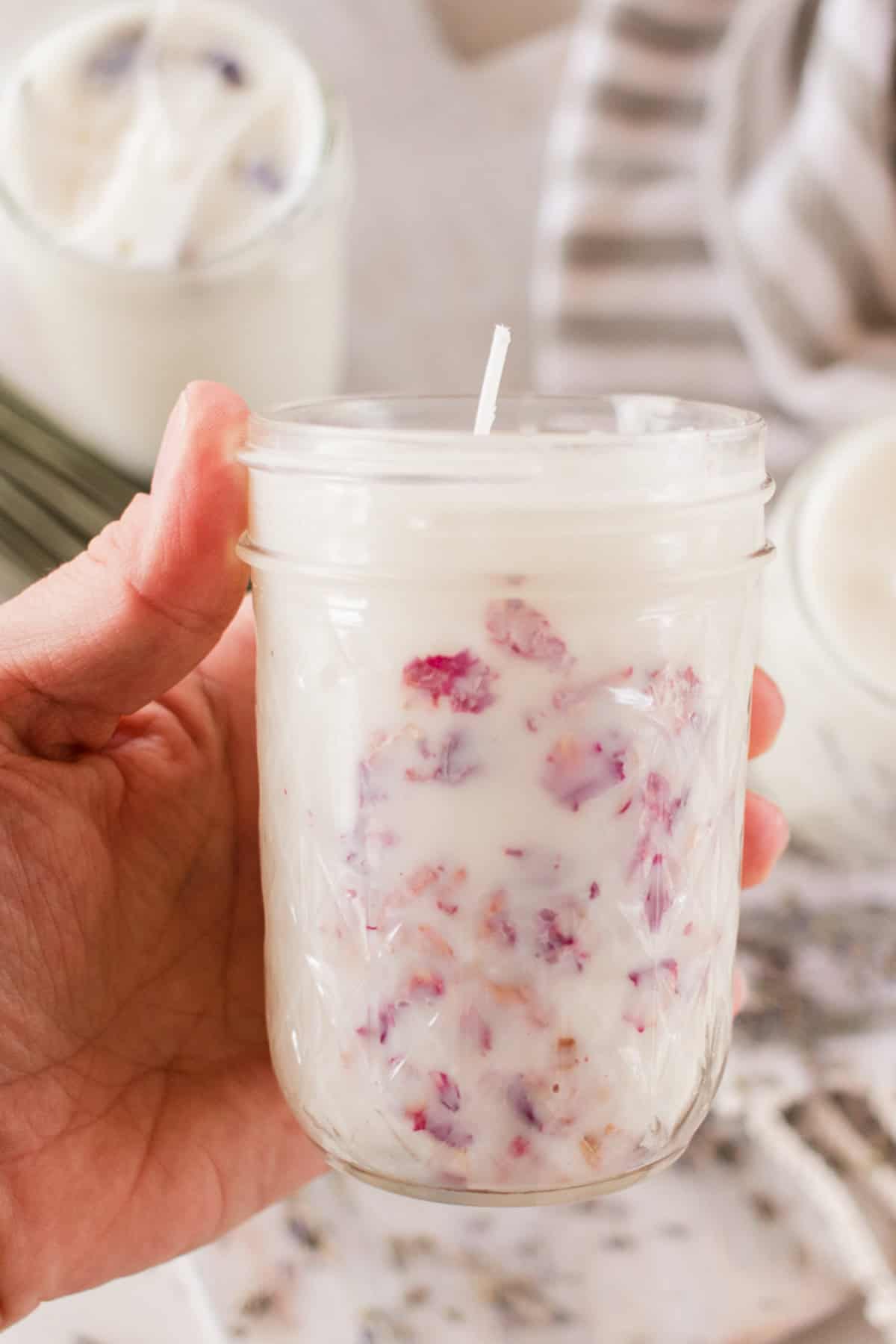 Holding a mason jar candle with pink dried flower petals.