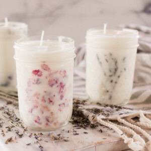Three mason jar candles on a white table with dried lavender;