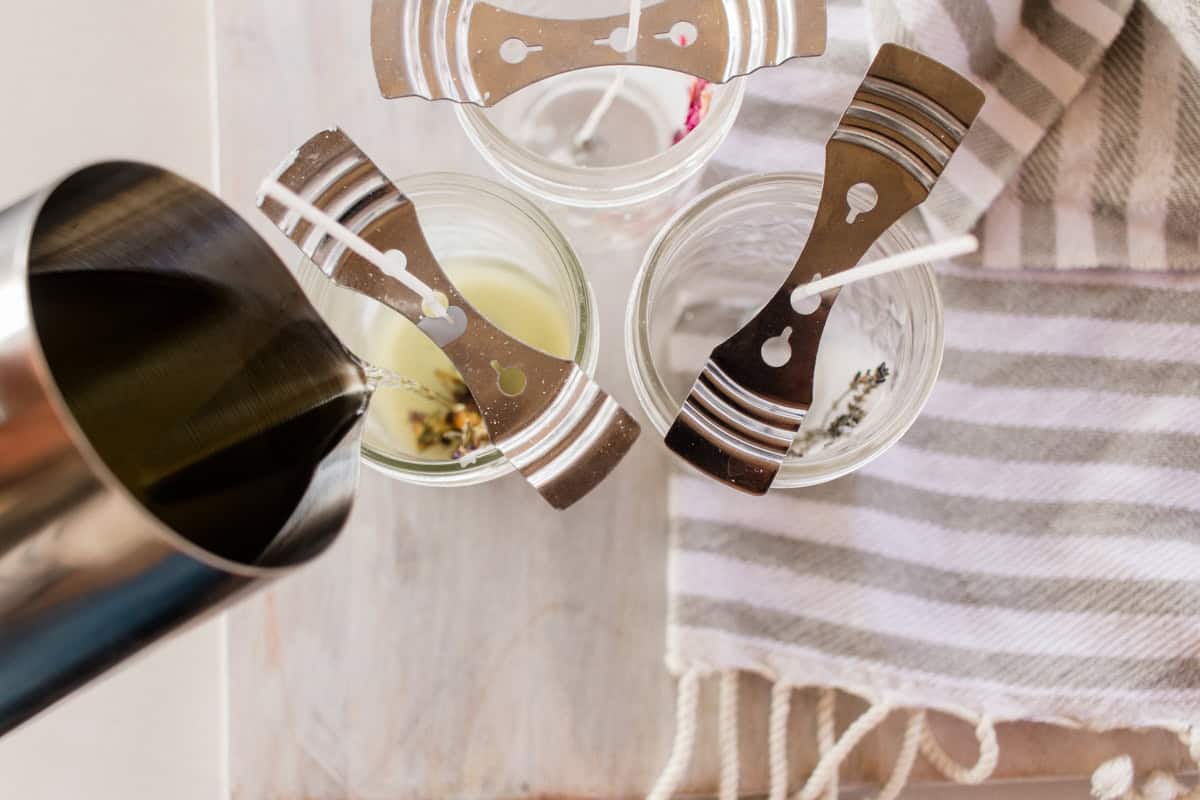 Pouring wax into mason jars with wick holder and candle wicks sticking out the top.