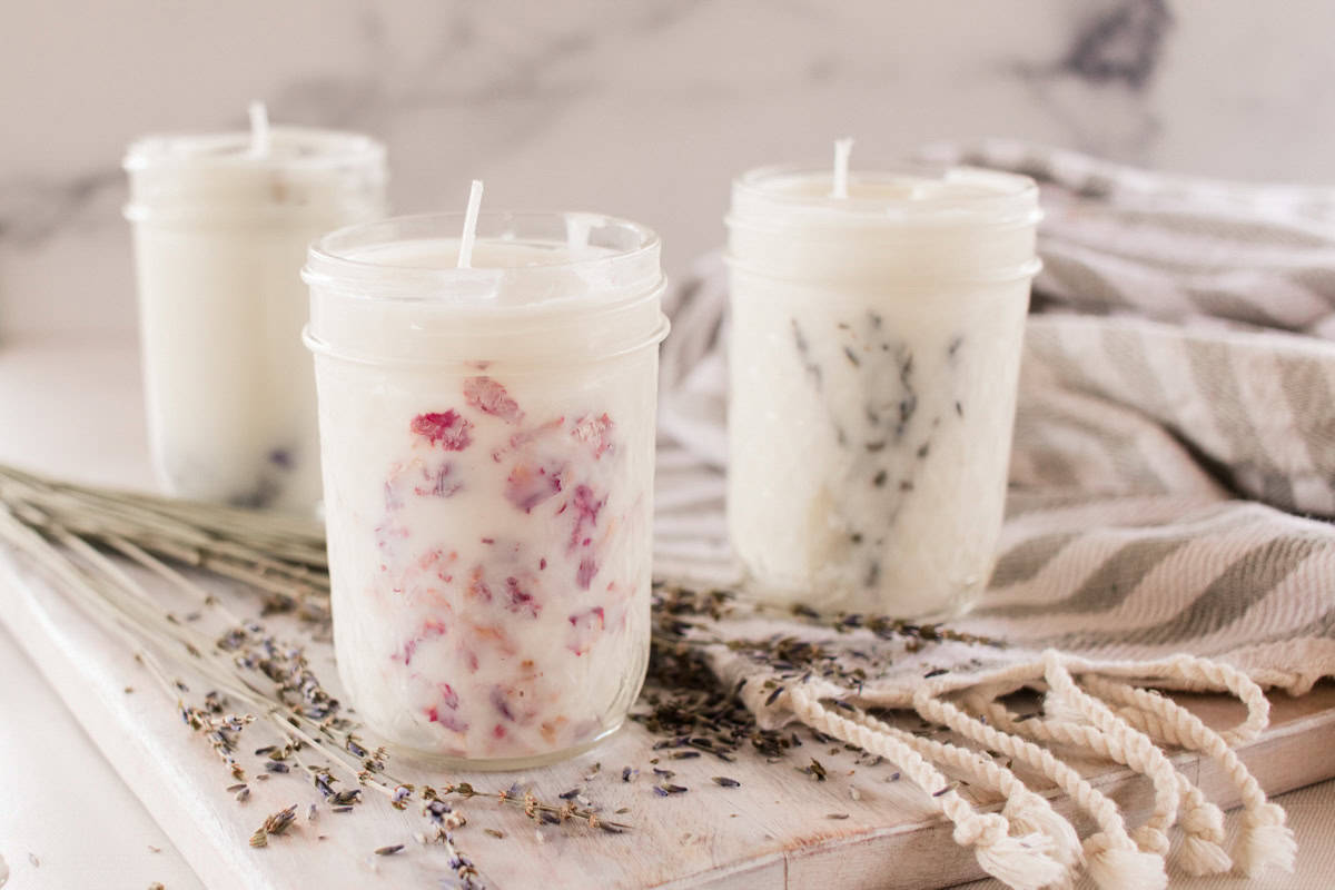 Three mason jar candles on a white table with dried lavender;
