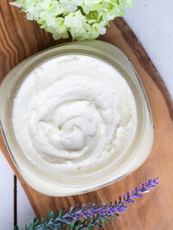 Homemade face moisturizer in a clear, wide mouth jar with lavender sprigs placed next to it.