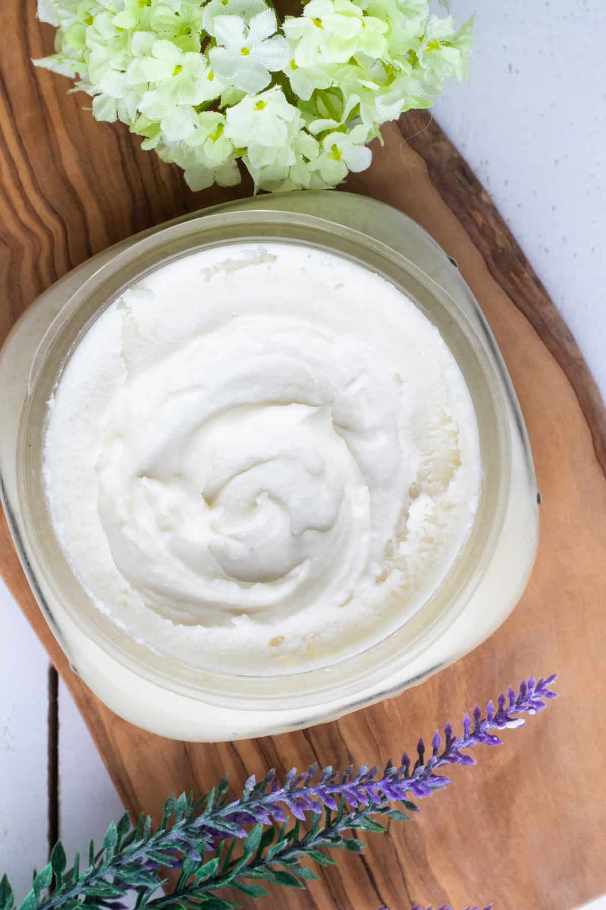 Homemade face moisturizer in a clear, wide mouth jar with lavender sprigs placed next to it. 