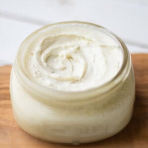 Small jar of homemade face moisturizer on a wooden tray.