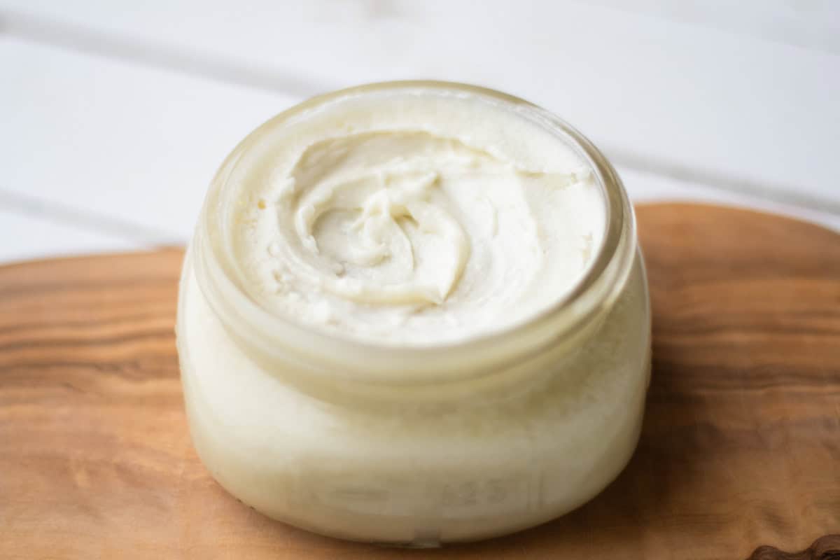 Small jar of homemade face moisturizer on a wooden tray.