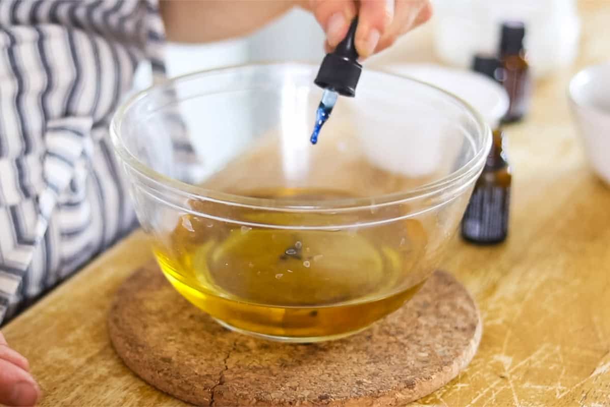 Dropping a few drops of yarrow pom essential oil into the melted oils.