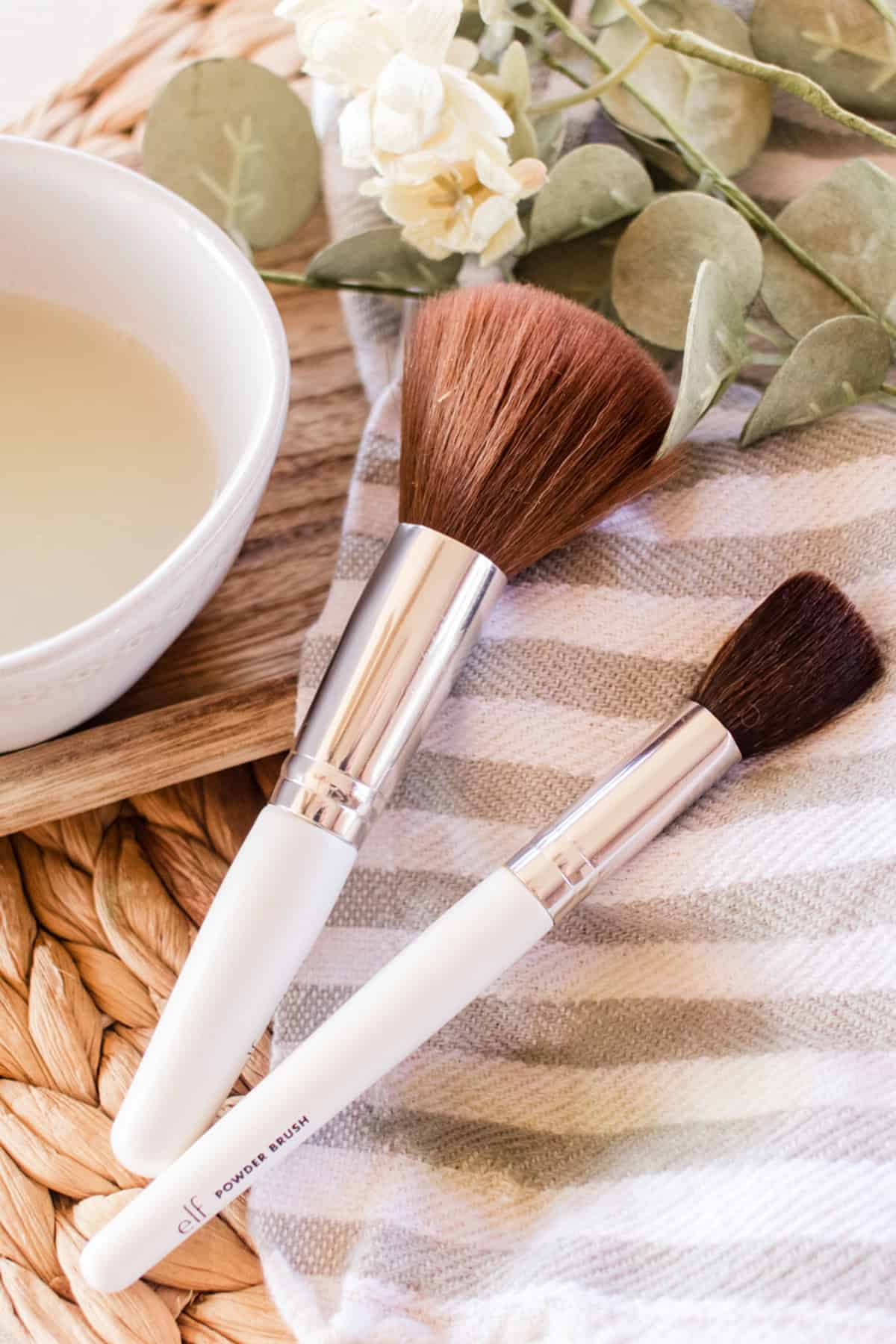 Makeup brushes with homemade makeup brush cleaner on a striped towel.