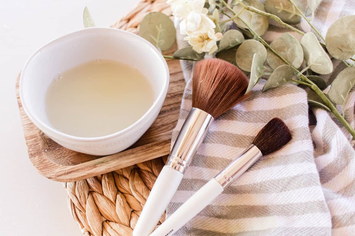 Makeup brushes on a towel with a bowl of makeup brush cleaner.