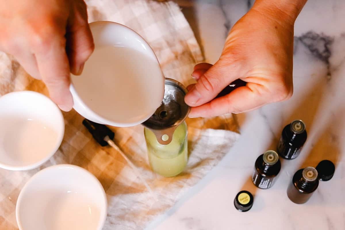 Pouring witch hazel into a glass spray bottle.