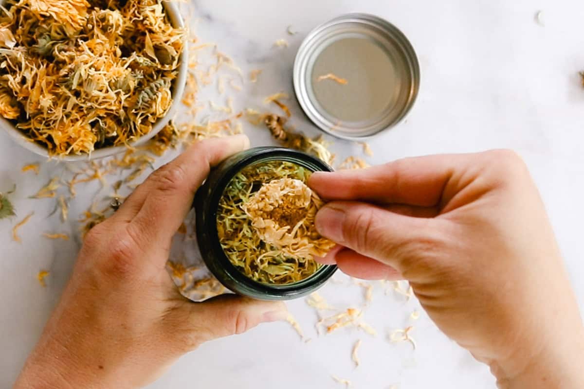Grabbing a pinch of dried calendula flowers out of a jar.
