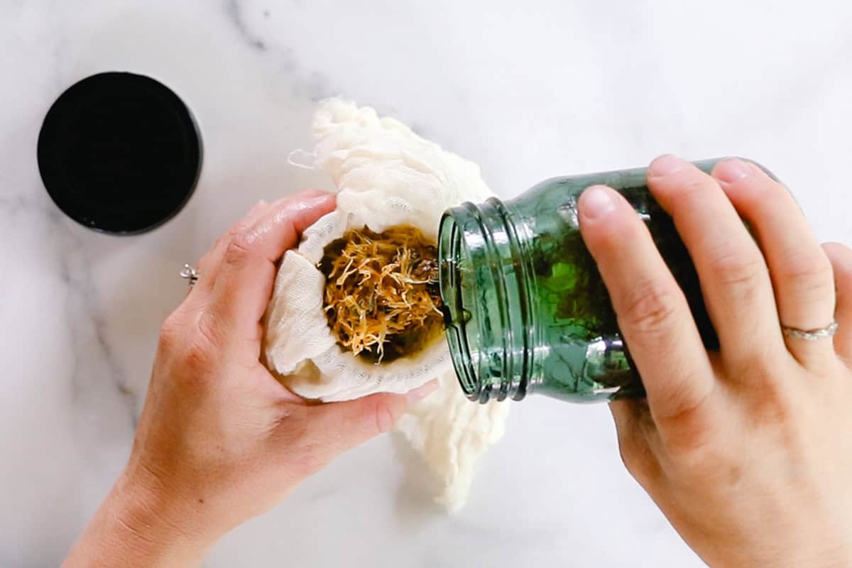 Pouring calendula oil into a cheesecloth to strain.