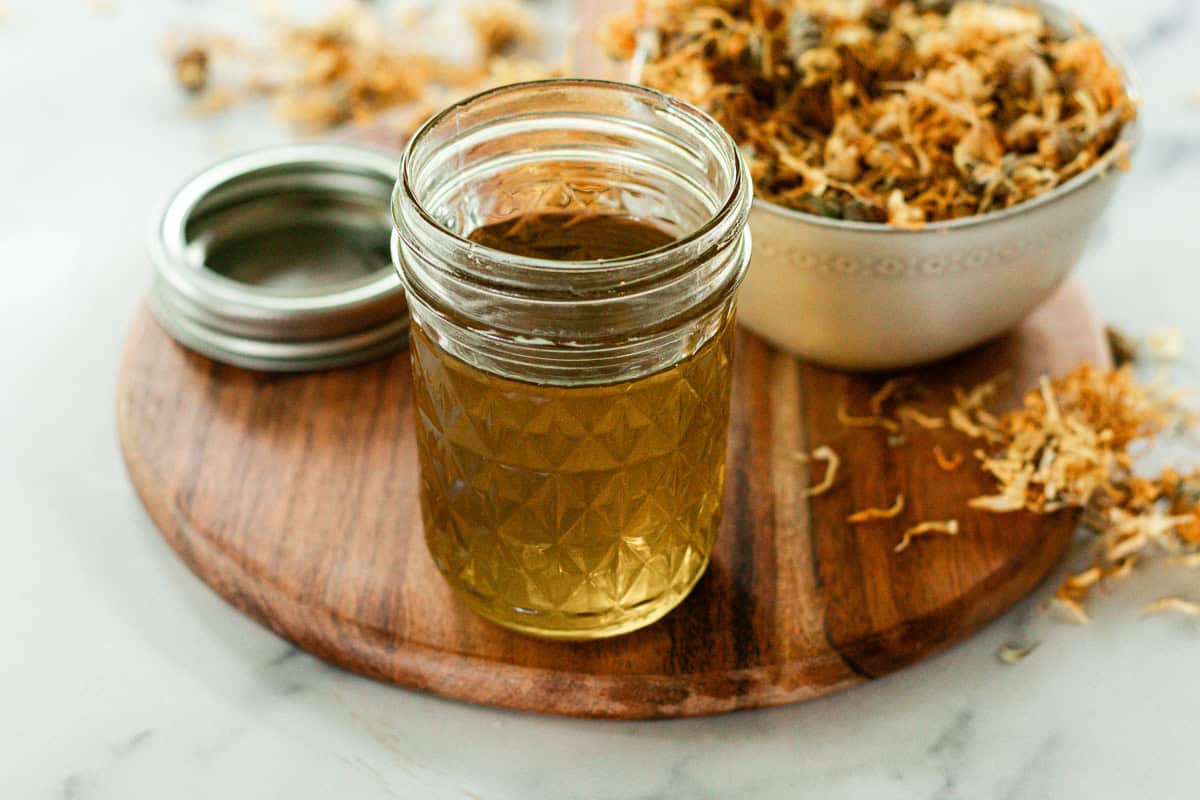 A jar of calendula oil and a bowl of dried calendula flowers.