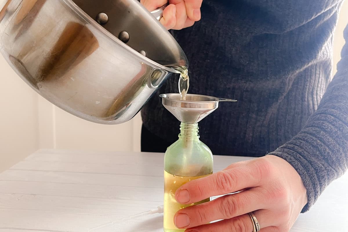 Pouring the cooled rosemary water into a clear spray bottle using a metal funnel. 