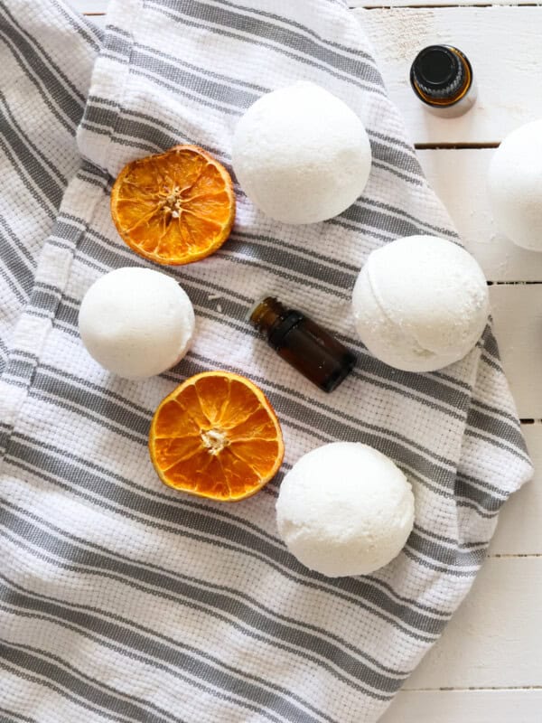 4 homemade bath bombs drying on a tea towel that is placed on top of a white shiplap table.