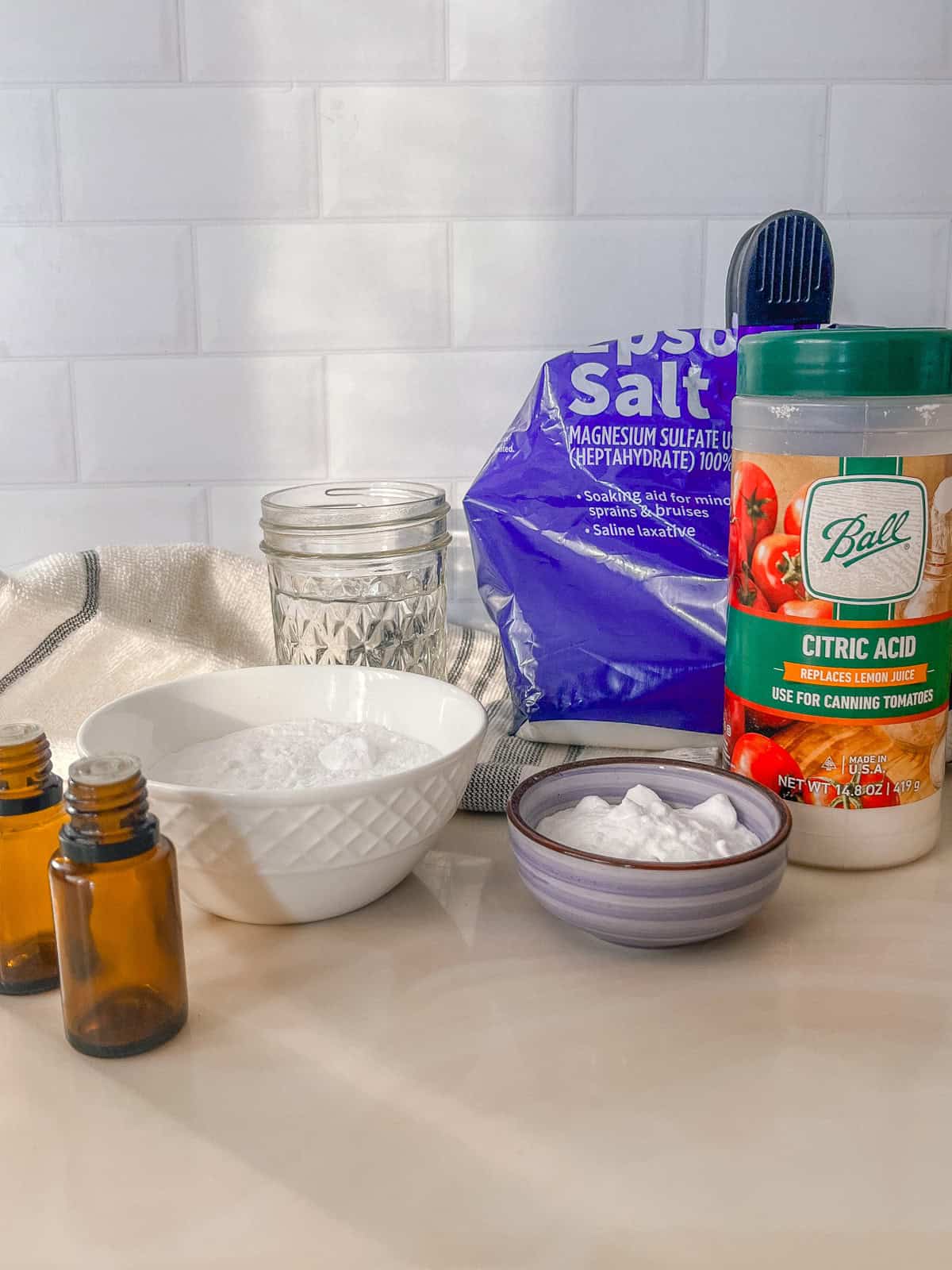 Ingredients for a bath bomb recipe measured out on a white marble vanity. 
