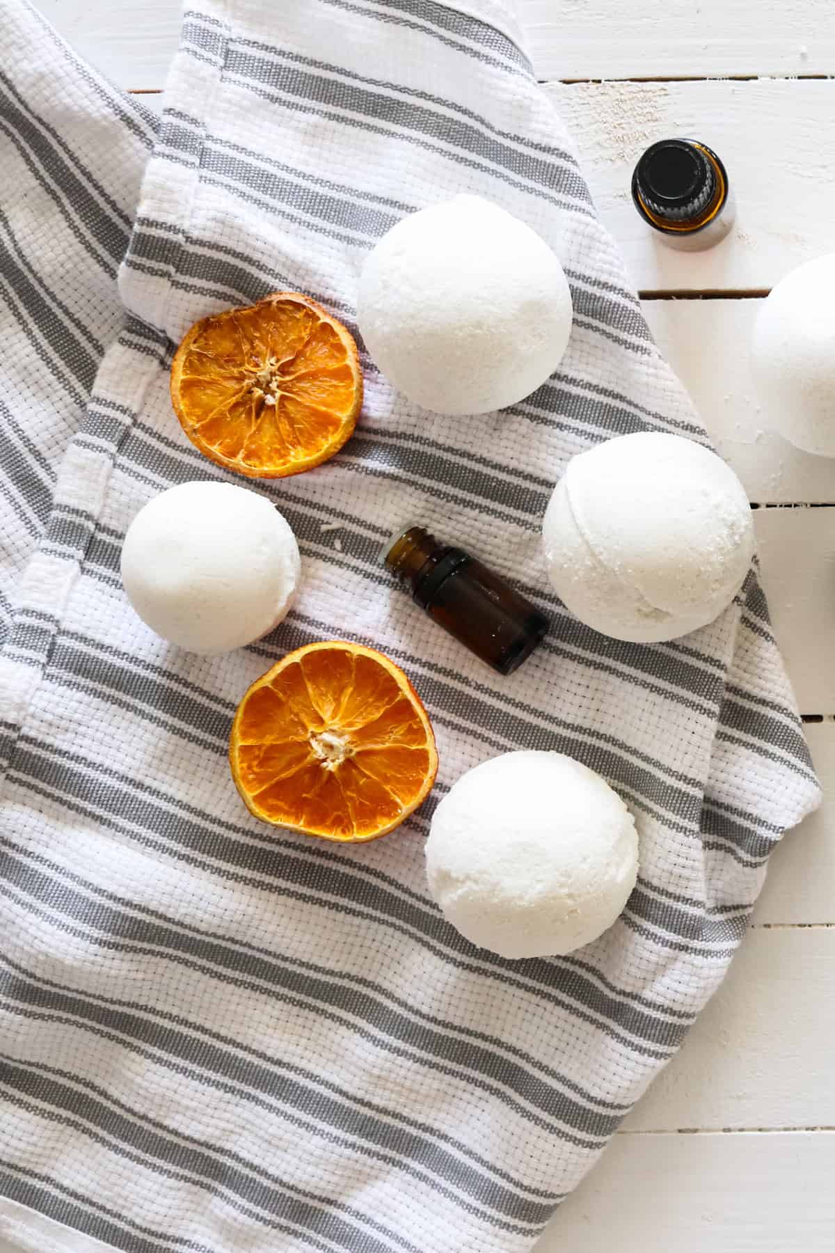 4 homemade bath bombs drying on a tea towel that is placed on top of a white shiplap table.