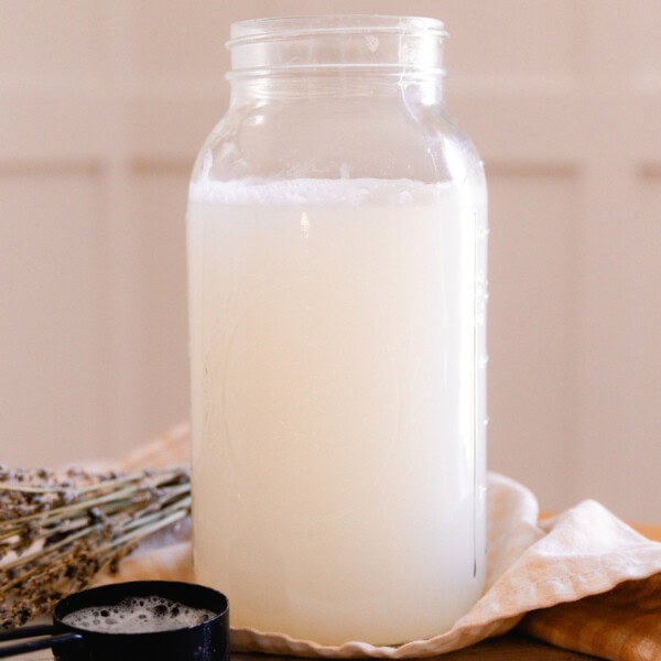 A mason jar with homemade laundry detergent next to dried lavender and a measuring cup.