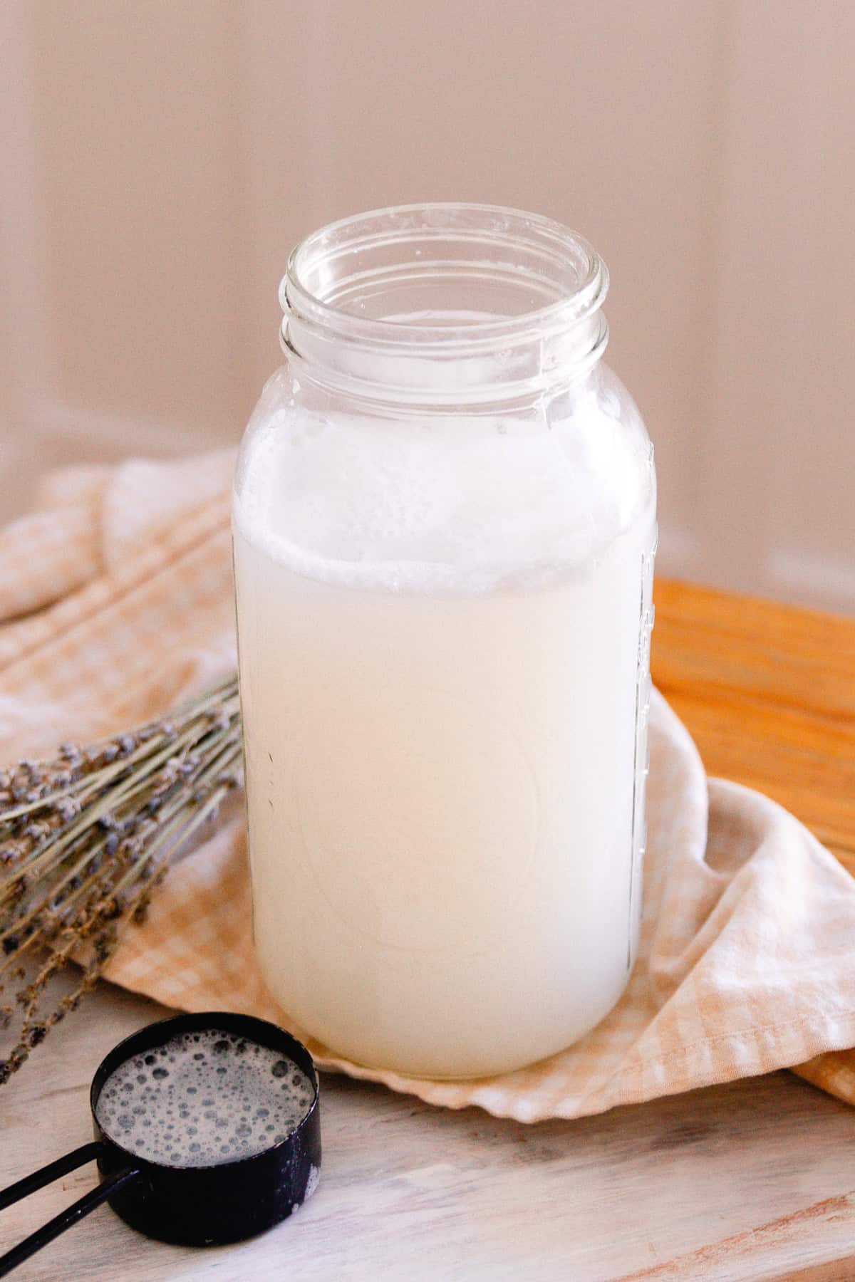 A jar of homemade laundry detergent with a measuring cup and dried lavender.
