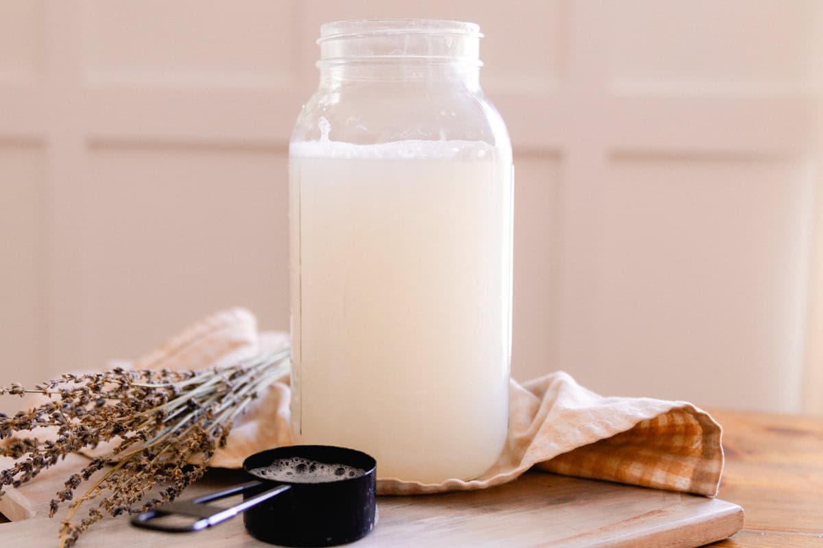A mason jar with homemade laundry detergent next to dried lavender and a measuring cup.