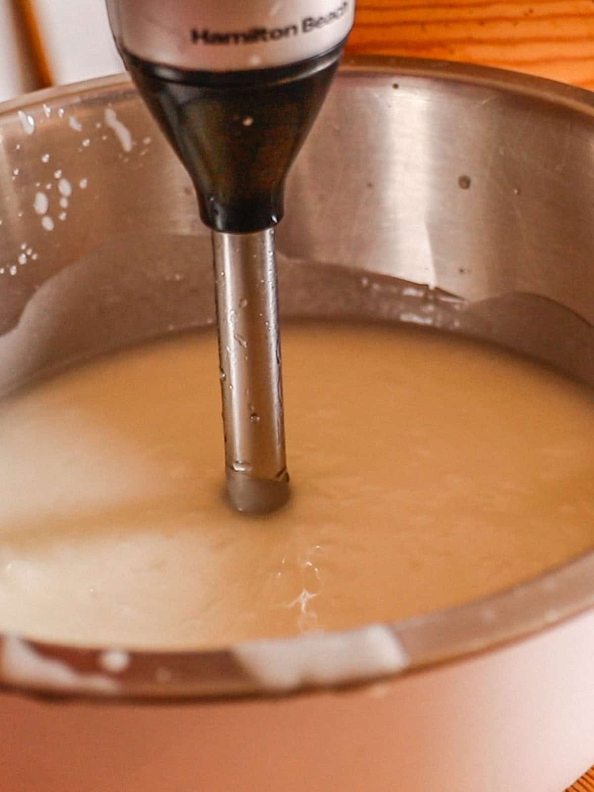 Using an immersion blender to blend soap mixture.