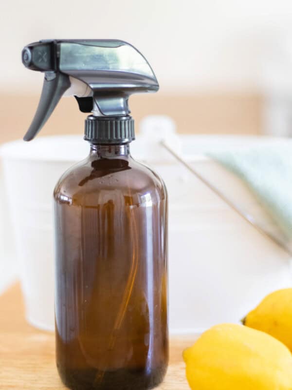 A bottle of all-purpose spray with lemons and a cleaning bucket.