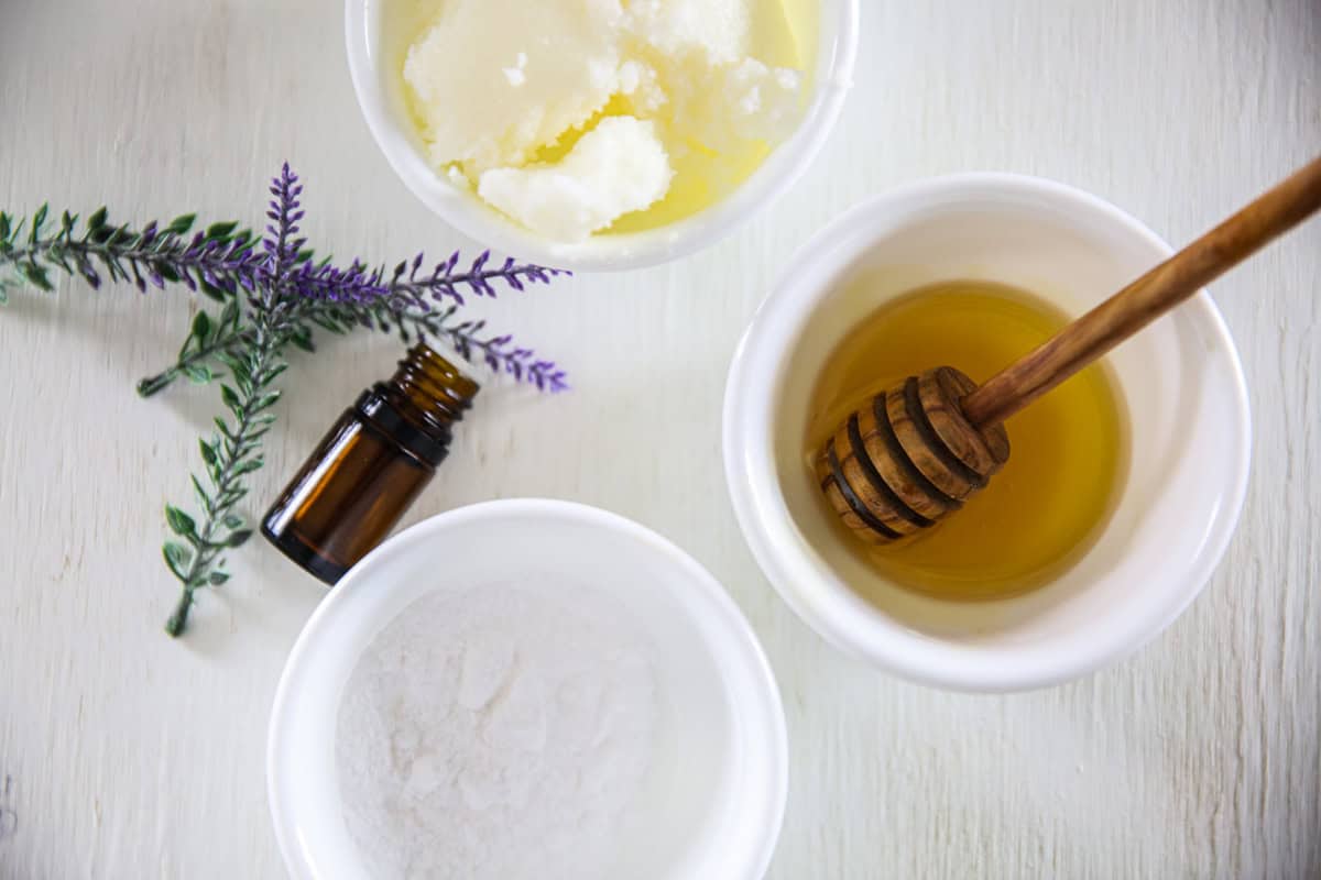 Bowls of honey, coconut oil, and baking soda next to a bottle of essential oil.