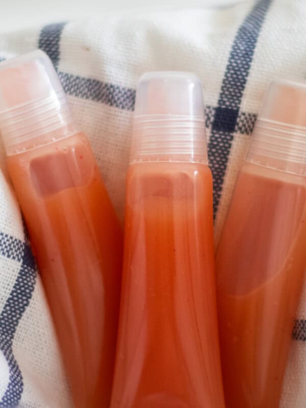 Three tubes of lip gloss on a blue and white towel.