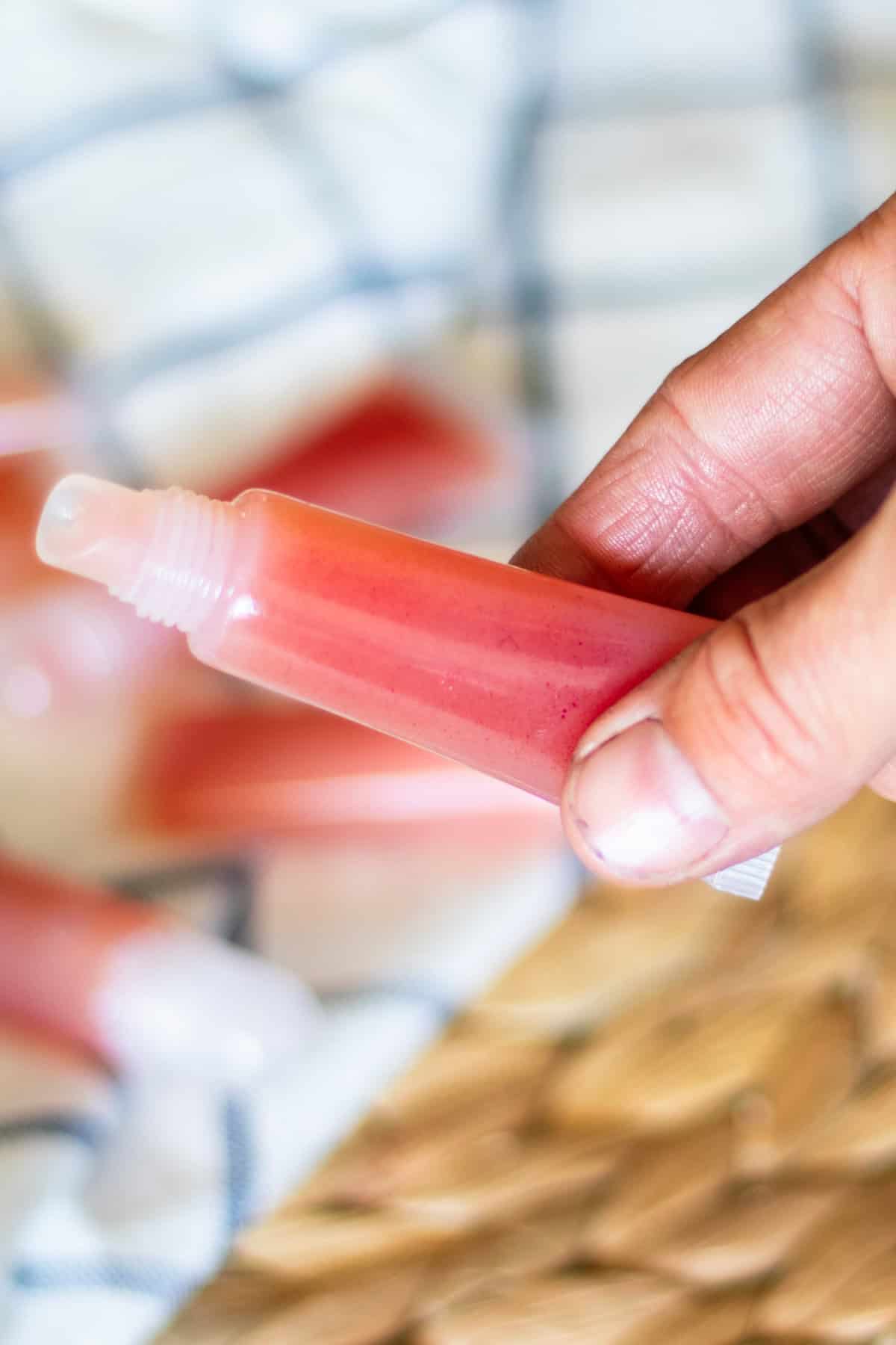 Holding a tube of DIY lip gloss over other tubes on a towel.