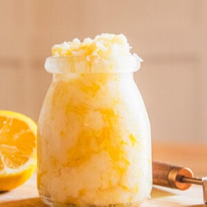 A jar of homemade hand scrub with a lemon half and a measuring spoon.